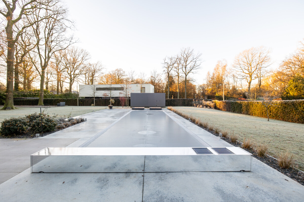 Piscine couverte par une structure métallique réfléchissante dans un jardin avec arbres dénudés et pelouse givrée, sous un ciel clair.