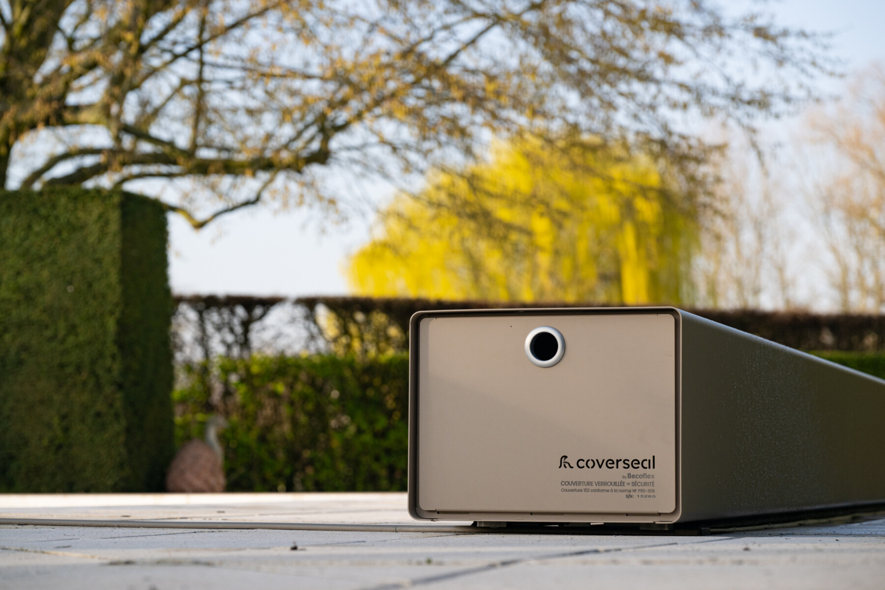 Vue d’ensemble de la piscine et du jardin, avec la couverture Coverseal et un espace détente sur une terrasse en bois entourée de végétation.
